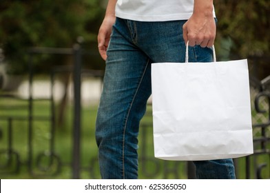 man with a white paper bag in hands on a park background. courier with a bag on the background of a green park