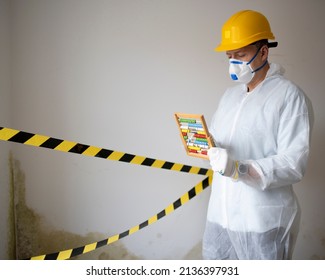 Man With White Protective Suit With Abacus Calculator, Slide Rule In Hand And Mouth Nose Mask In Front Of Yellow Black Barrier Tape In Front Of Wall With Mildew