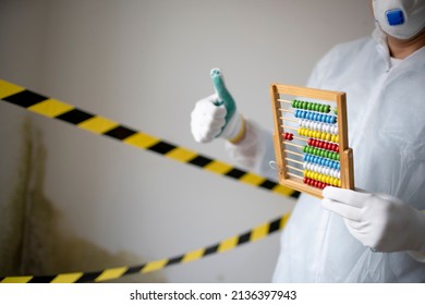 Man With White Protective Suit With Abacus Calculator, Slide Rule In Hand And Mouth Nose Mask In Front Of Yellow Black Barrier Tape In Front Of Wall With Mildew