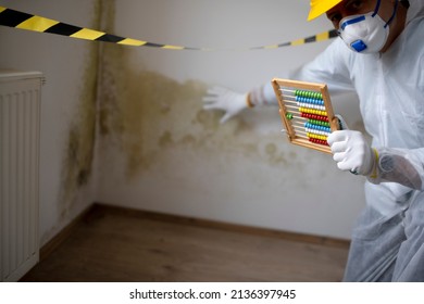 Man With White Protective Suit With Abacus Calculator, Slide Rule In Hand And Mouth Nose Mask In Front Of Yellow Black Barrier Tape In Front Of Wall With Mildew