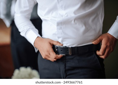 A man in a white shirt and black belt is adjusting his pants. Concept of formality and attention to detail, as the man is making sure his outfit is properly fitted - Powered by Shutterstock