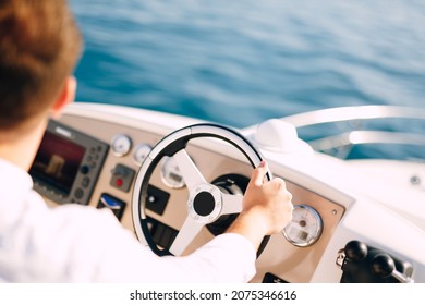 Man in a white shirt is driving a white motor boat. Close-up