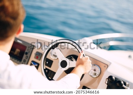 Man in a white shirt is driving a white motor boat. Close-up