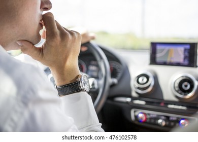 A Man In A White Shirt With An Expensive Watch, Driving A Car And Watching The GPS. He Seems To Be Unsure Where To Go.