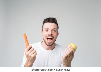 A man in a white shirt isolated on a light background holding carrot and apple. Vegetarian preparing a meal. Smiling guy loves fruits and vegetables. - Powered by Shutterstock