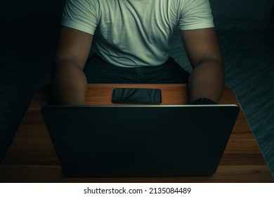A man in a white shirt sits on a laptop in a dark room. with light shining down. internet concept addiction.topview.