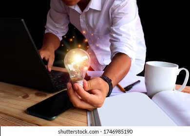 A man in a white shirt stretched out with one hand holding a shining lamp. And the other side pressing the notebook keyboard, creative concept with sparkling light bulbs