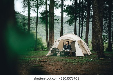 a man with a white snow peak tent in a pine forest with mountains and green grass - Powered by Shutterstock