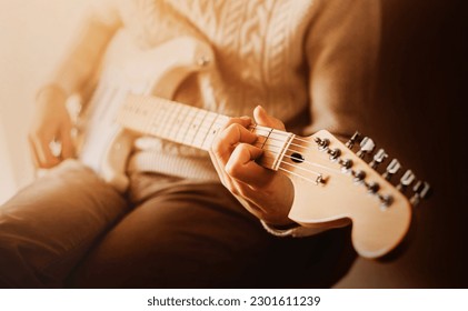 A man in a white sweater plays rock music on a white electric guitar on a sunny morning. Performing music on a six-string guitar. Art and inspiration.