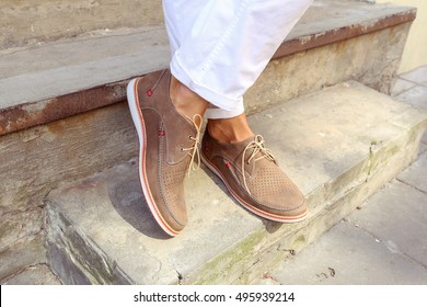Man in white trousers on the steps in the city. Men's summer fashion, stylish men's shoes. Brown Perforated suede summer shoes with laces