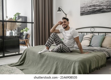 A Man In White Tshirt And Plaid Pants Sitting On Bed At Home