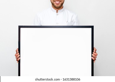 Man In White Uniform Holding A Picture Frame Or Poster For Mock Up. Doctor Or Chef Smiling And Showing Empty Frame, Business And Advertisement Concept - Man With White Blank Board