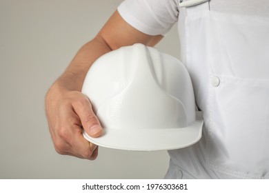 A man in a white work uniform holds a white helmet in his hands. Mock-up.