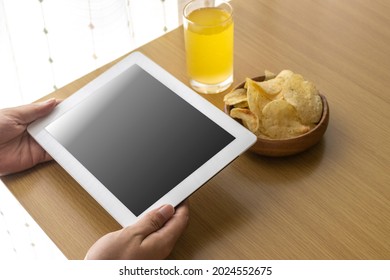 A man who eats snacks during breaks and uses a tablet device