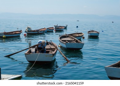 The Man Who Goes Fishing With His Small Boat In The Sea.Man Going Fishing Trying To Untie The Rope Of The Boat. There Are Other Empty Fishing Boats In The Sea.