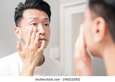 A man who looks in the mirror and checks the condition of his skin - Shutterstock ID 1960232002