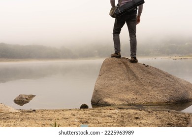 Man whose legs are only seen facing the lake in the morning where the water still gives off fog