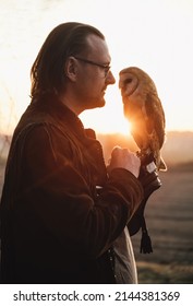 Man and wild bird over sunset sky in field looking on each other Owl symbol of power, wisdom wealth, learning person in eye glasses, vision problems. Nature and human partnership, friendship