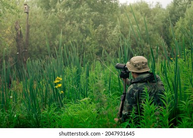 man wildlife researcher makes field observation with a spotting scope standing among the tall grass - Shutterstock ID 2047931645