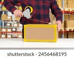 Man will pack box. Packer guy uses dispenser with tape. Packing parcel at warehouse. Cropped packer at work. Wrapping cardboard box with tape. Person works as packer in distribution center