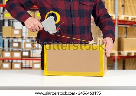 Man will pack box. Packer guy uses dispenser with tape. Packing parcel at warehouse. Cropped packer at work. Wrapping cardboard box with tape. Person works as packer in distribution center