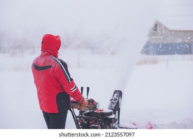 Man In Windproof Cleans, Clears Snowdrifts And Drifts In Blizzard Outside The City. Particles Of Snow And Drifts Fly Everywhere. Selective Focus, Inclement Weather.