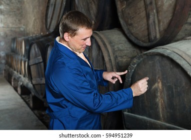 Man wine technician expert working in storage with wooden barrels