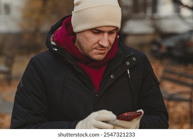 Man in winter attire checks smartphone outdoors in a park during autumn. - Powered by Shutterstock