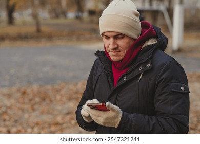 Man in winter attire checks smartphone outdoors in a park during autumn. - Powered by Shutterstock