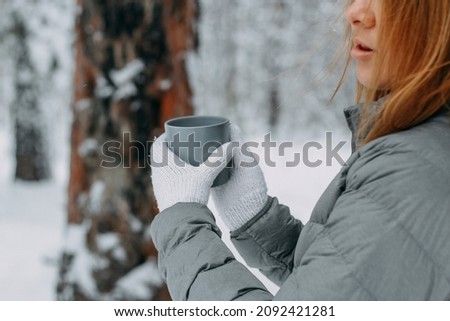 A man in the winter in the forest holds a gray mug with a hot drink in his hands. Warm and cozy in the winter park.selective focus.