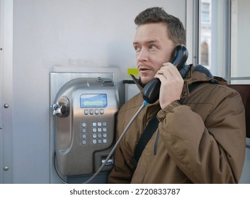 A man in winter jacket using public payphone. Urban retro moment with cold-weather style and nostalgic tech.