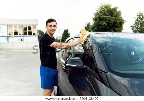 a\
man wipes the car from water with microfiber from stains. cleaning\
the car after washing. electric car and its\
cleaning