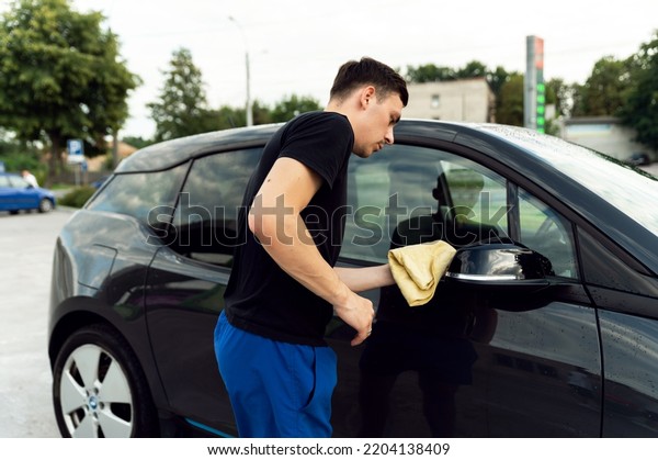 a\
man wipes the car from water with microfiber from stains. cleaning\
the car after washing. electric car and its\
cleaning
