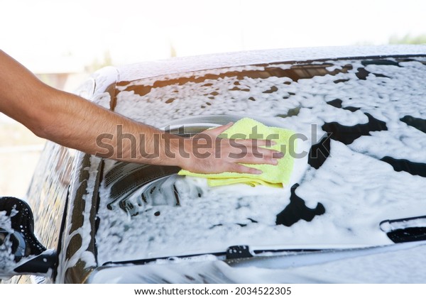 a man\
wipes the foam on the car with a rag. car\
wash