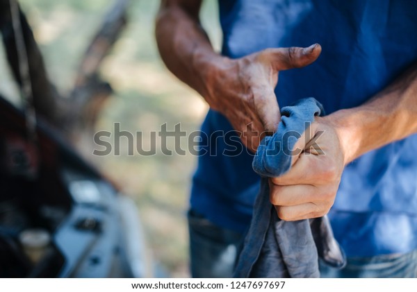 Man wipes\
his hands with a cloth in front of\
car