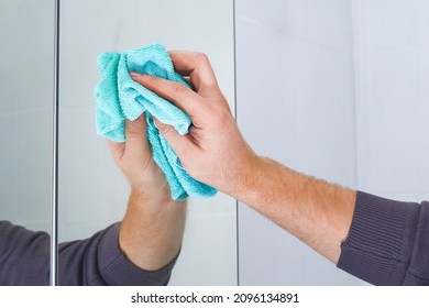 A man wipes a mirror cabinet in the bathroom with a rag. Cleaning of the house, bathroom. - Powered by Shutterstock