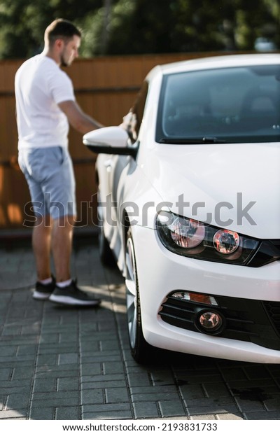 Man is wiping the car with a microfiber\
cloth. Contactless self-service car wash. Personal car care\
cleaning outside. Concept disinfection and antiseptic cleaning of\
vehicle, covid-19 and\
coronavirus