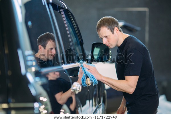 The\
man is wiping with a cloth body of a brilliant\
car.