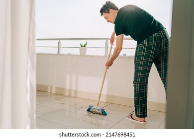 Man Wiping Floor With The Mop. Janitor Male Washing The Dirty Floors. Guy Mopping The Balcony On A Sunny Day. Person Doing Home Chores. Young Fellow Using Cleaning Equipment To Dust The Surface.