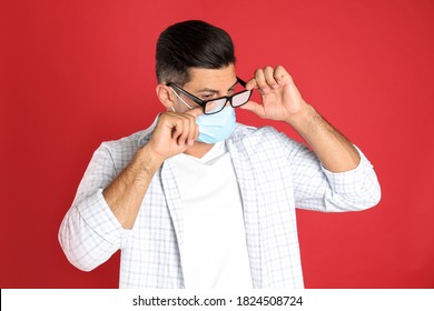 Man Wiping Foggy Glasses Caused By Wearing Medical Mask On Red Background