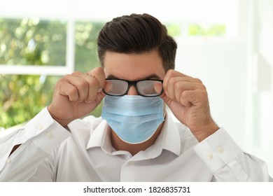 Man Wiping Foggy Glasses Caused By Wearing Medical Mask Indoors, Closeup