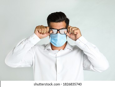 Man Wiping Foggy Glasses Caused By Wearing Medical Mask On Light Background