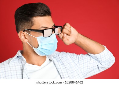 Man Wiping Foggy Glasses Caused By Wearing Medical Mask On Red Background