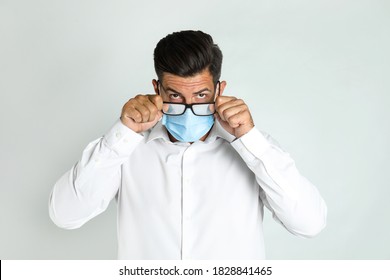 Man Wiping Foggy Glasses Caused By Wearing Medical Mask On Light Background