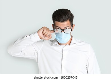 Man Wiping Foggy Glasses Caused By Wearing Medical Mask On Light Background