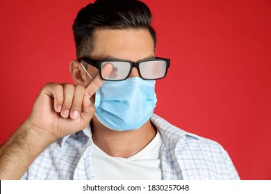 Man Wiping Foggy Glasses Caused By Wearing Medical Mask On Red Background