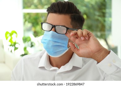 Man Wiping Foggy Glasses Caused By Wearing Medical Mask Indoors, Closeup