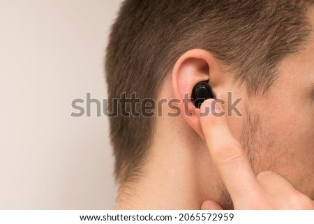 A man with a wireless earphone in his ear. The man turns on the wireless earpiece with his finger. Space for text, copy space