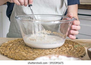 A Man Without A Face In An Apron Holds A Whisk In His Hands And Kneads Dough For Baking In The Kitchen. Authentic Home Cooking Hobby, Home Baker. Man Cooking In The Kitchen At Home