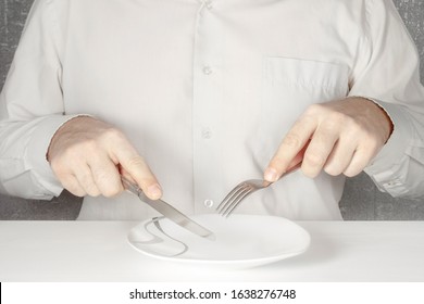 A Man Without A Face In A Gray Shirt Sits At A Table With A Knife And A Fork In His Hands And Eats Imaginary Food From An Empty Plate.